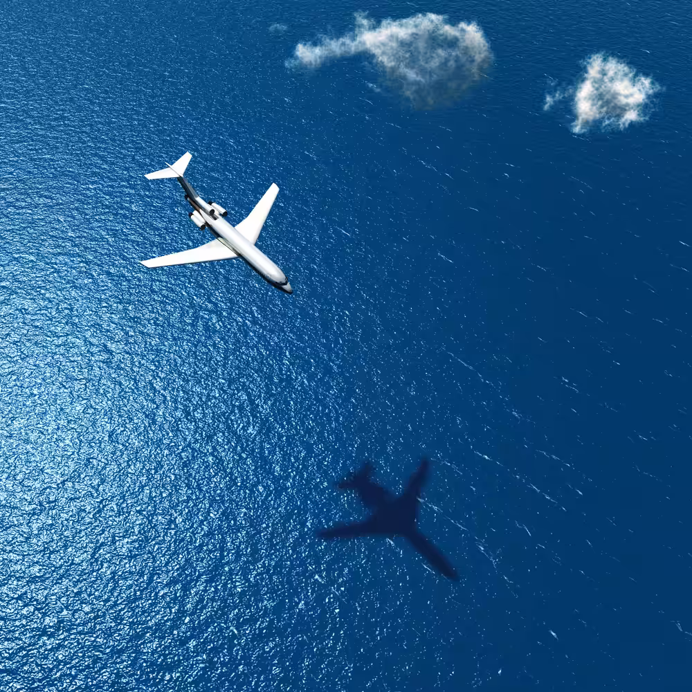 Commercial passenger jet flying over open ocean with shadow cast on deep blue water below