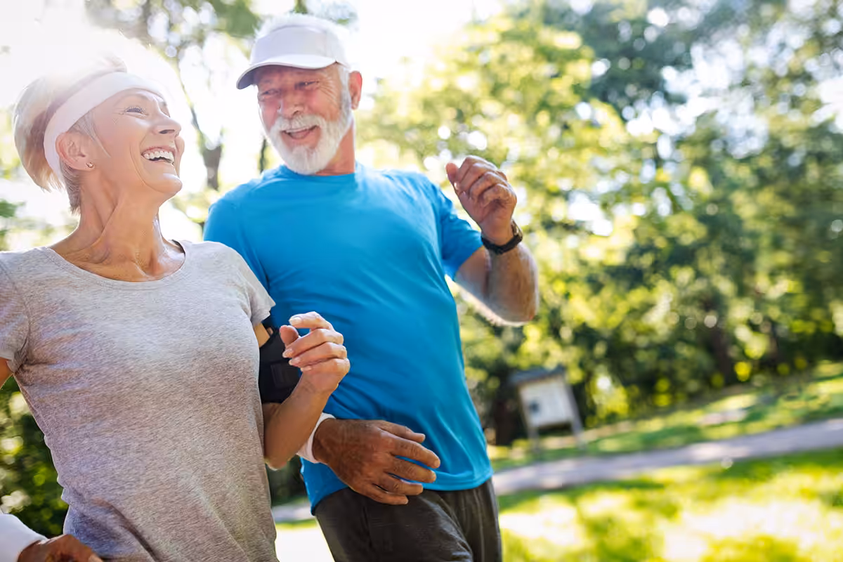 Retired couple jogging together in a sunny park, staying active and healthy in their 60s with ASEBP MyRetiree Plan coverage