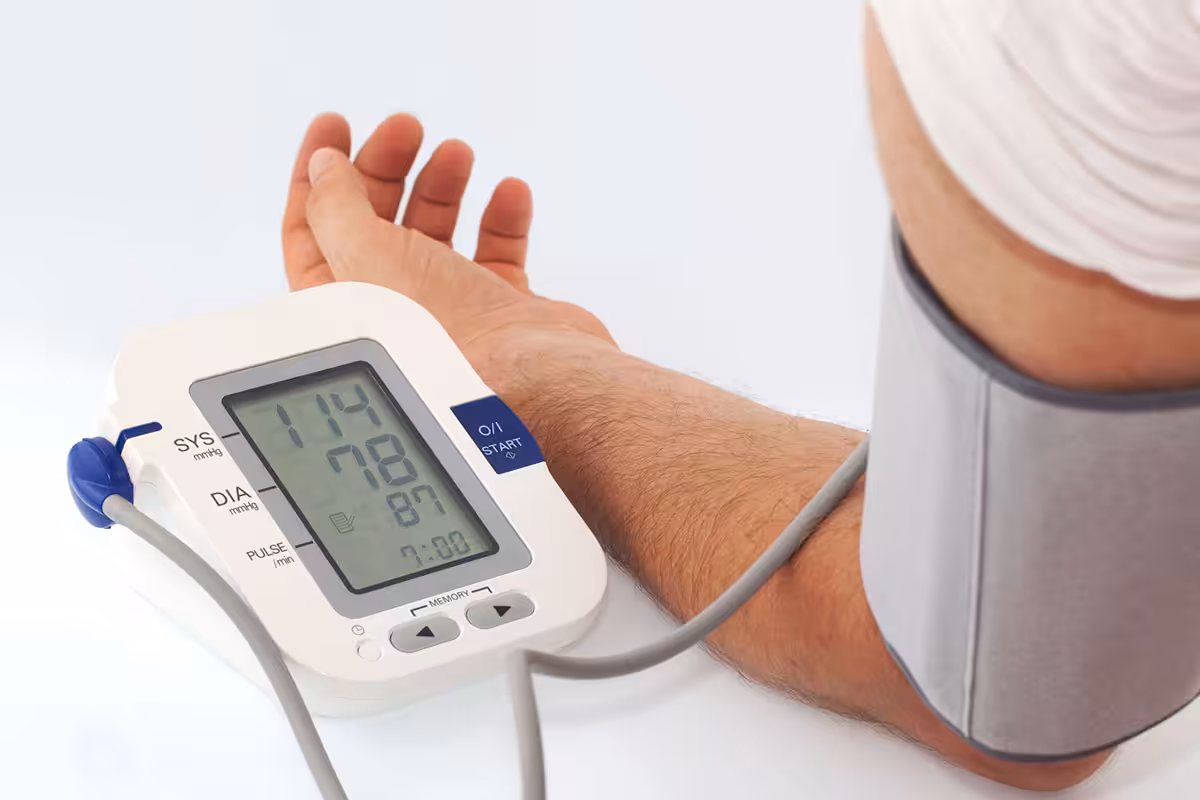 Digital blood pressure monitor displaying 114/78 mmHg systolic and diastolic readings with arm cuff on adult forearm