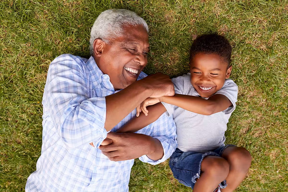 Grandfather and grandson laughing together on green grass, enjoying active retirement with ASEBP MyRetiree Plan coverage