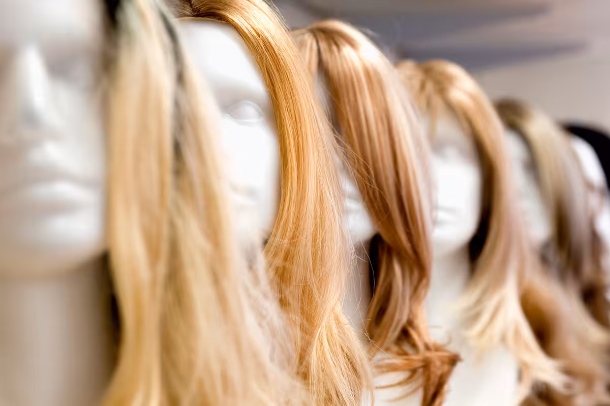 Row of mannequin heads displaying long blonde and auburn hairpieces covered under ASEBP MyRetiree Plan benefits