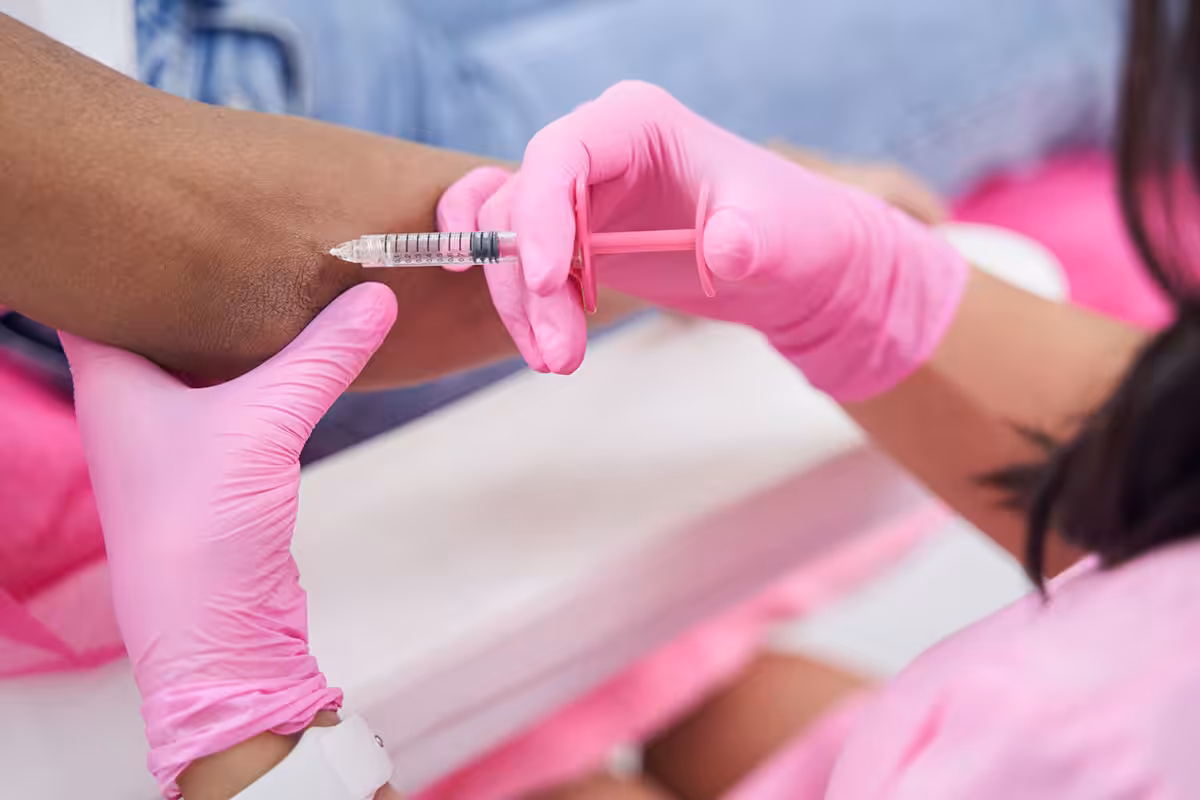Healthcare professional in pink gloves administering a joint injectable treatment into a patient's arm at a medical clinic
