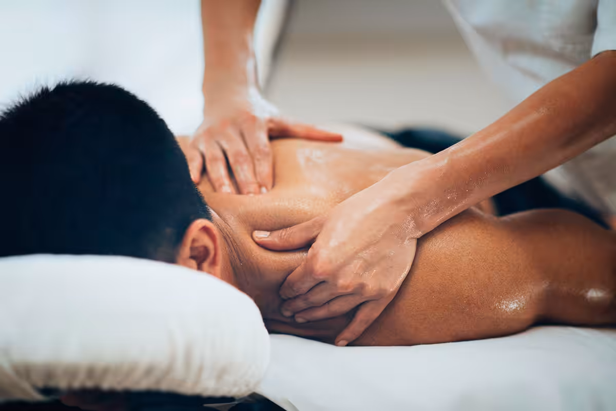 Professional massage therapist performing deep tissue massage on client's upper back and shoulders in a clinical spa setting
