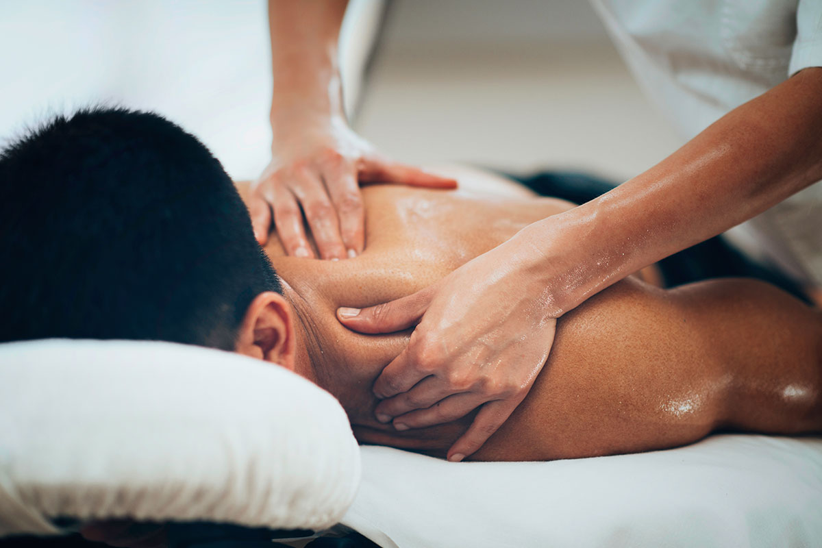 Professional massage therapist performing deep tissue massage on client's upper back and shoulders in a clinical spa setting