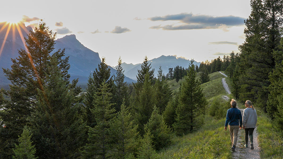 Retired Alberta educator couple embracing on a hillside, watching their family enjoy an outdoor gathering with travel coverage peace of mind