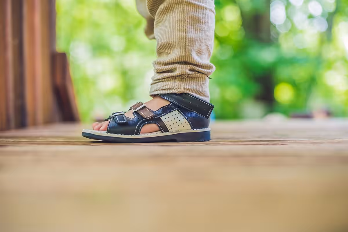 Child's foot in navy leather orthopedic sandal on wooden deck, representing orthopedic shoe coverage under ASEBP MyRetiree Plan