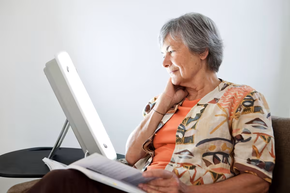 Senior woman sitting with a light therapy lamp, taking advantage of her retiree health benefits coverage