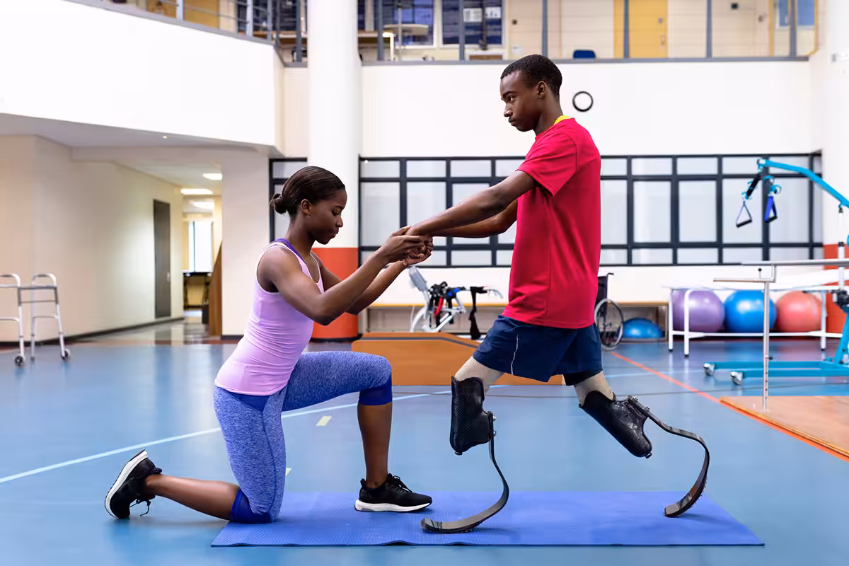 Rehabilitation specialist guiding prosthetic limb user through balance and walking exercises in a modern therapy facility