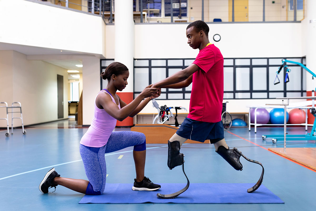 Rehabilitation specialist guiding prosthetic limb user through balance and walking exercises in a modern therapy facility