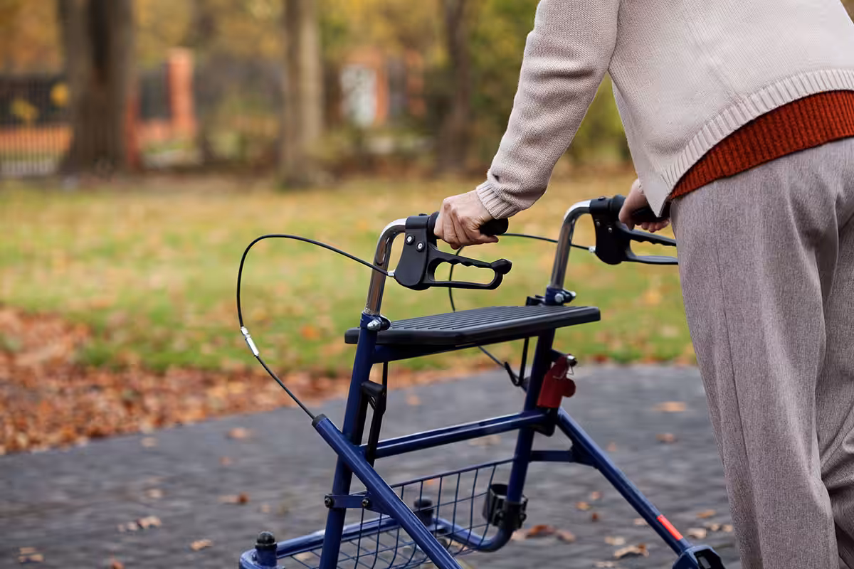 Senior using a blue rollator walker with hand brakes and storage basket during an autumn outdoor walk