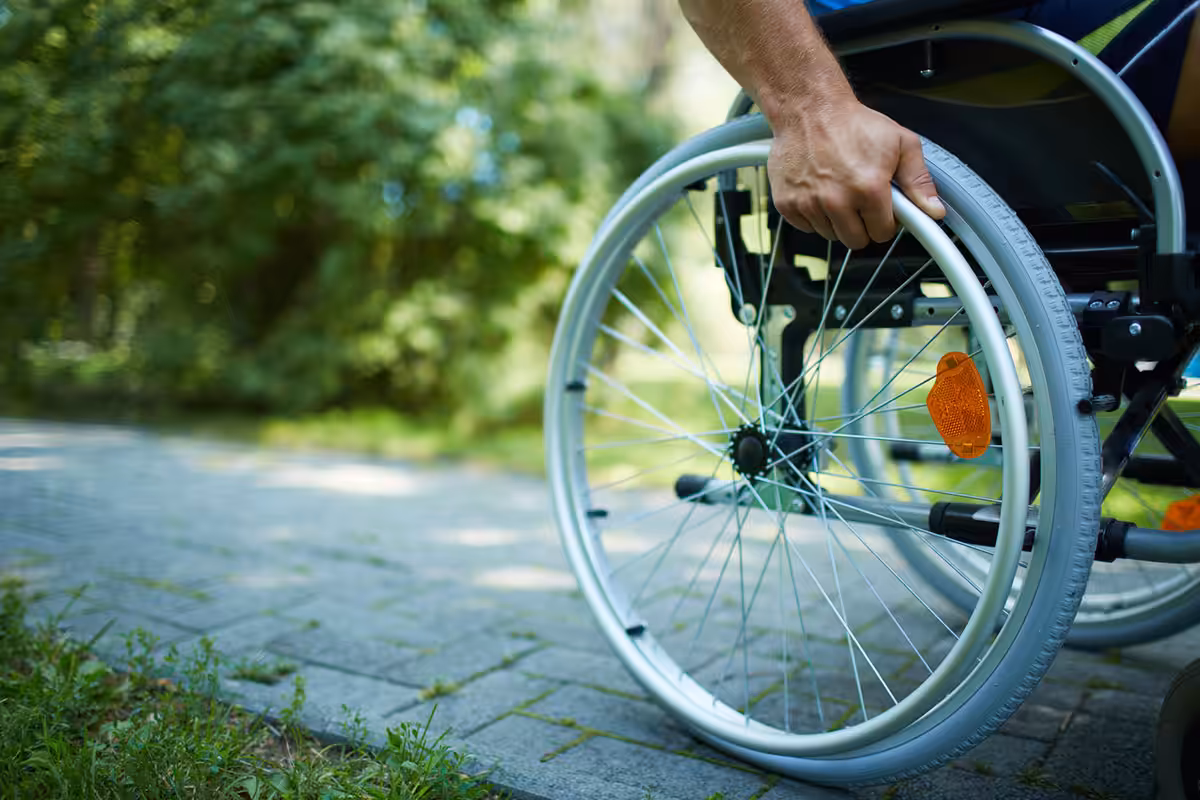 Person self-propelling a manual wheelchair along an outdoor stone pathway, gripping the hand rim