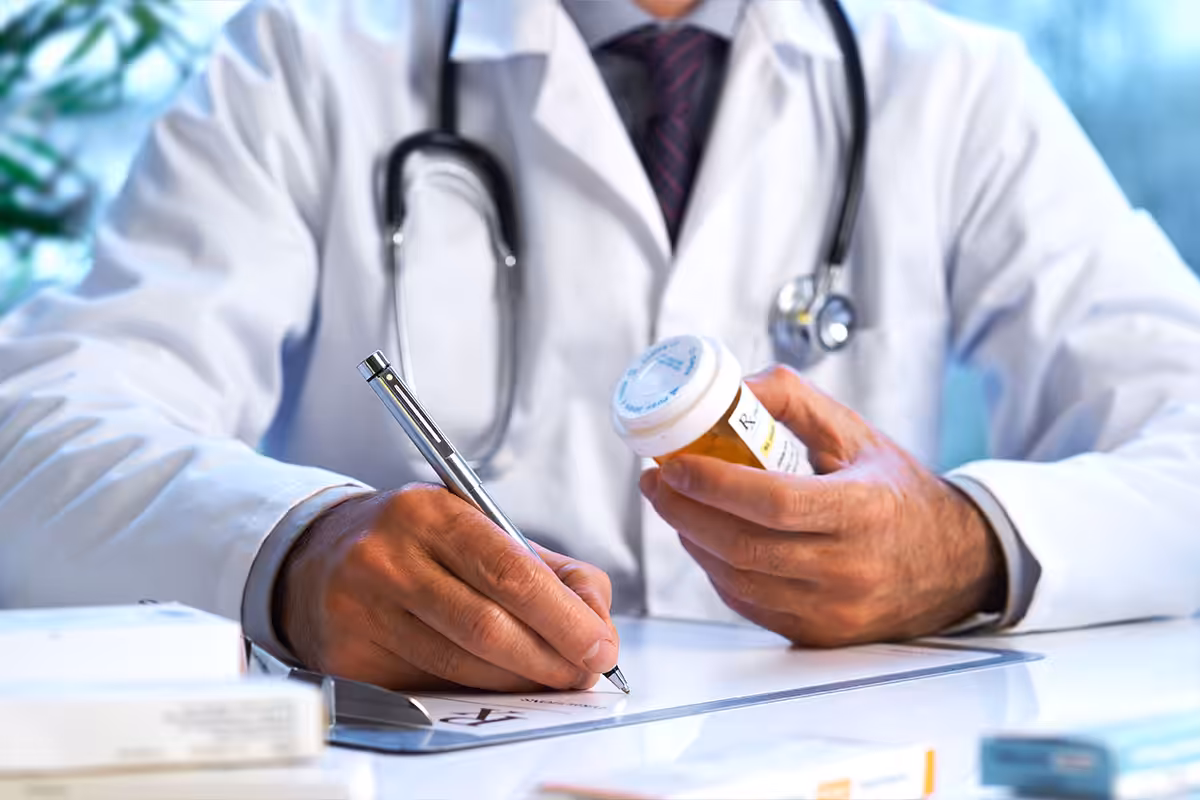 Doctor writing a prescription while reviewing a biosimilar drug bottle, with medical reference guides on desk