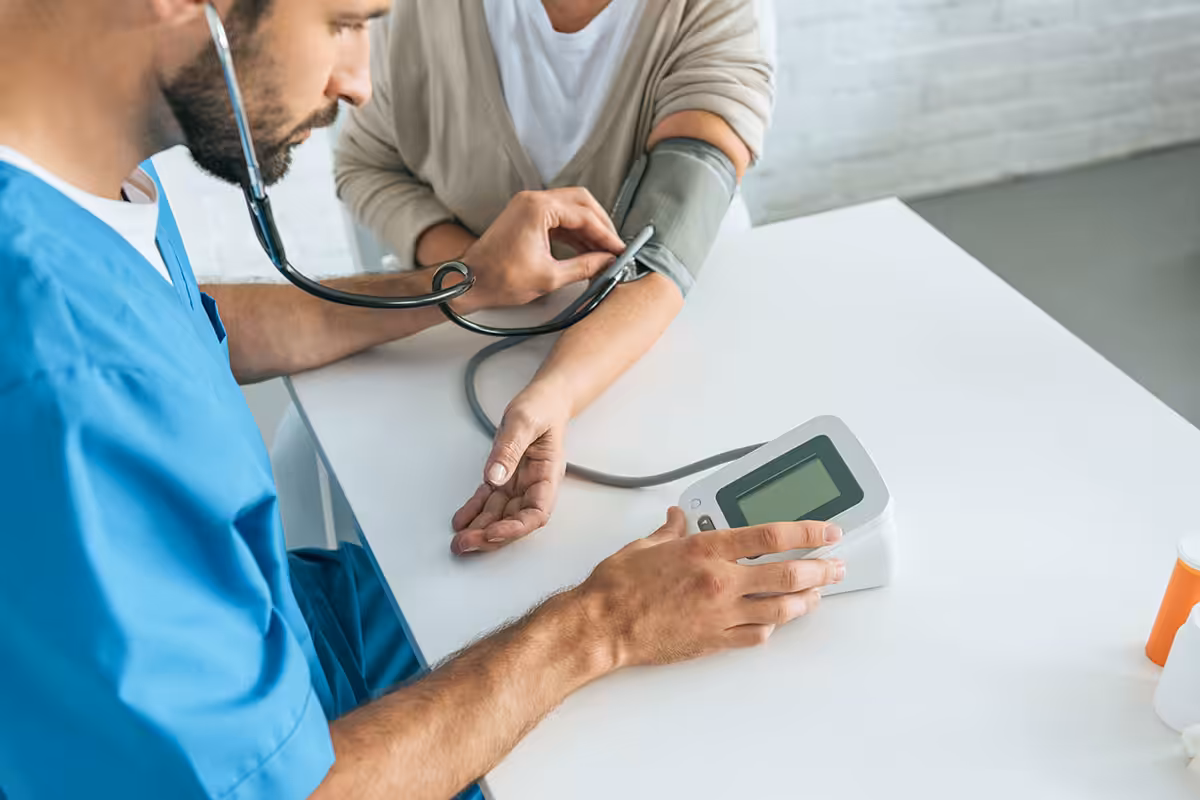 Clinician using digital sphygmomanometer and stethoscope to monitor patient blood pressure for medication review