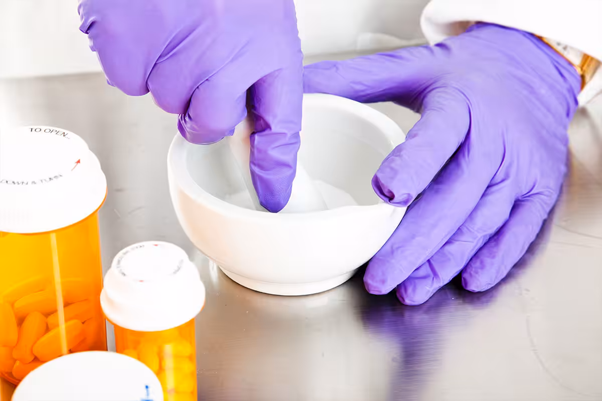 Compounding pharmacist mixing custom prescription medication using mortar and pestle with prescription bottles nearby