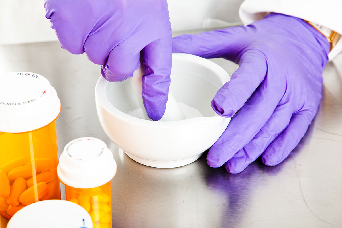 Compounding pharmacist mixing custom prescription medication using mortar and pestle with prescription bottles nearby