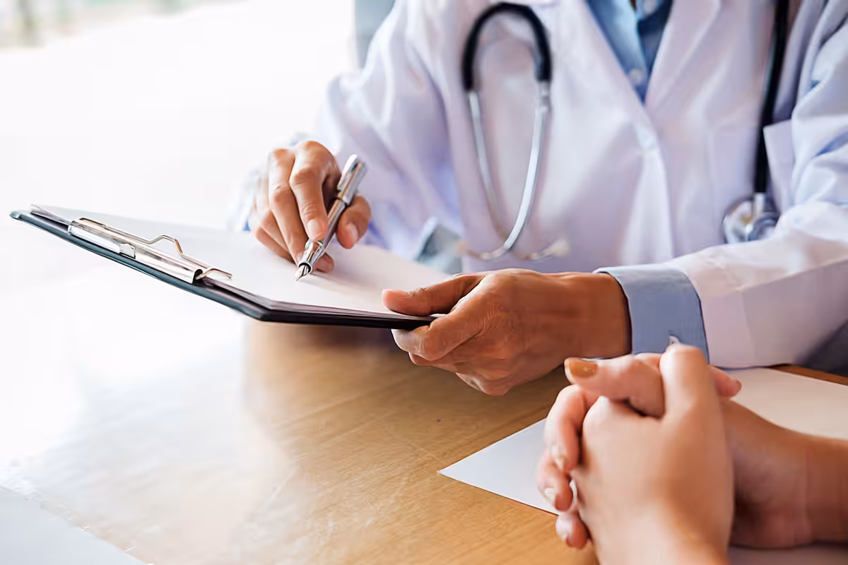 Doctor writing notes on clipboard during patient consultation for specialty drug authorization in Alberta