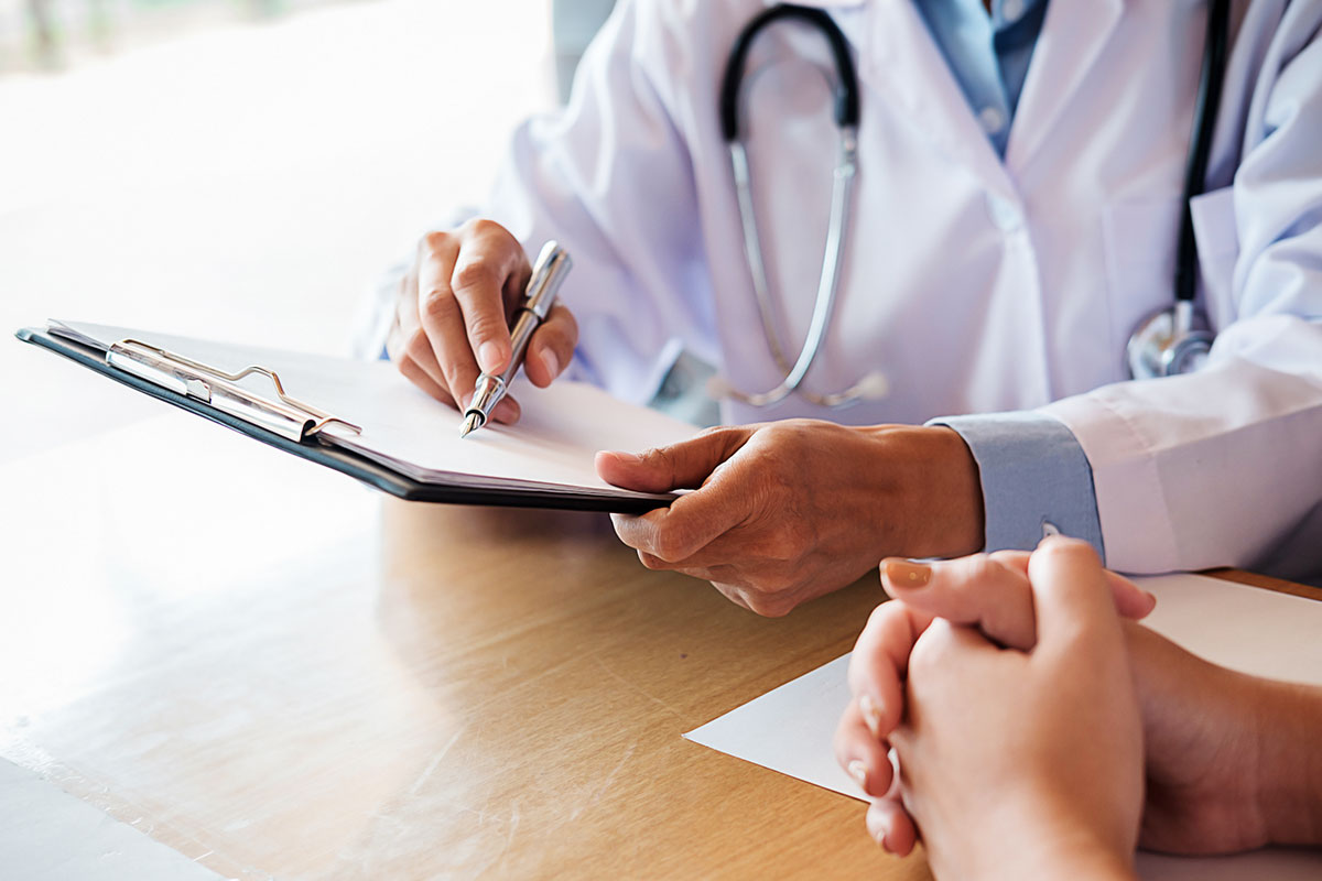 Doctor writing notes on clipboard during patient consultation for specialty drug authorization in Alberta