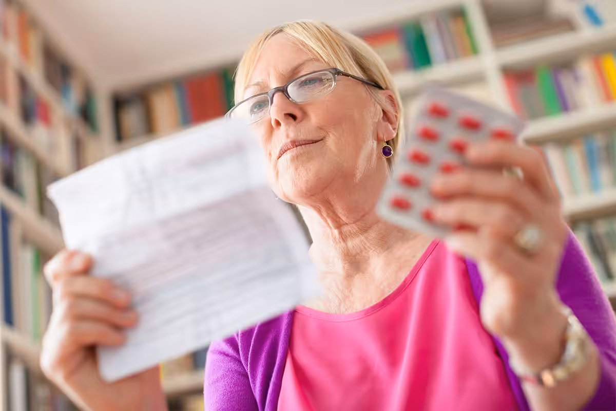 Retired woman comparing prescription medication leaflet with blister pack of pills at home
